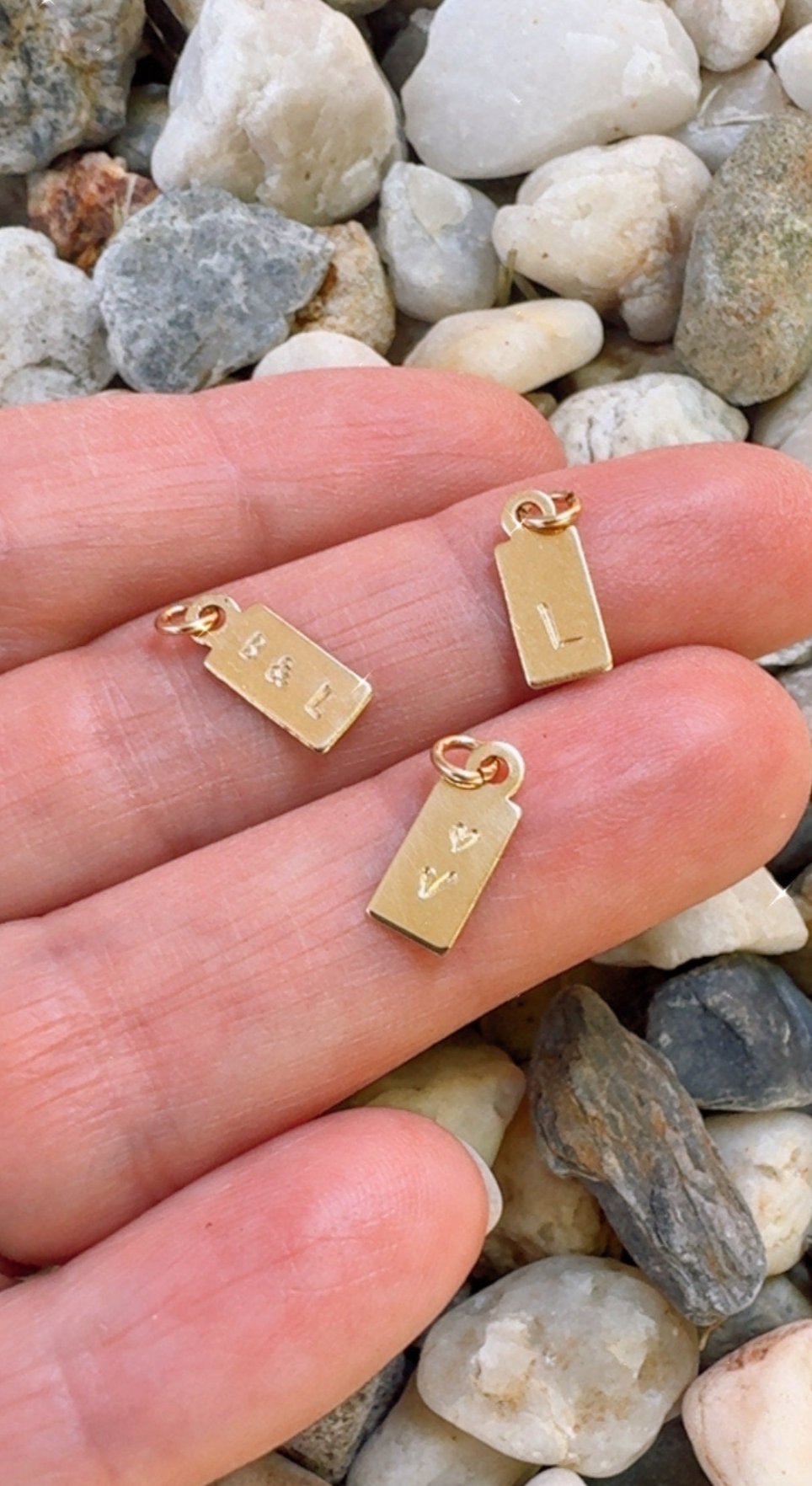 Woman holding three mini gold filled tags on hand to show the actual size of the charms